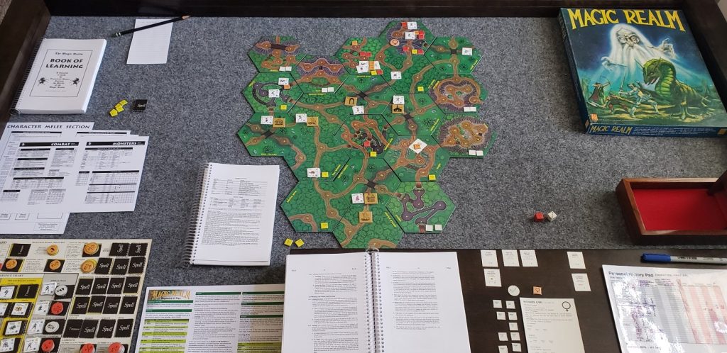The board game Magic Realm setup on my game table. The map tiles in the center are surrounded by the game box at the top right, the player area at the bottom right, and various manuals and player aids on the left.